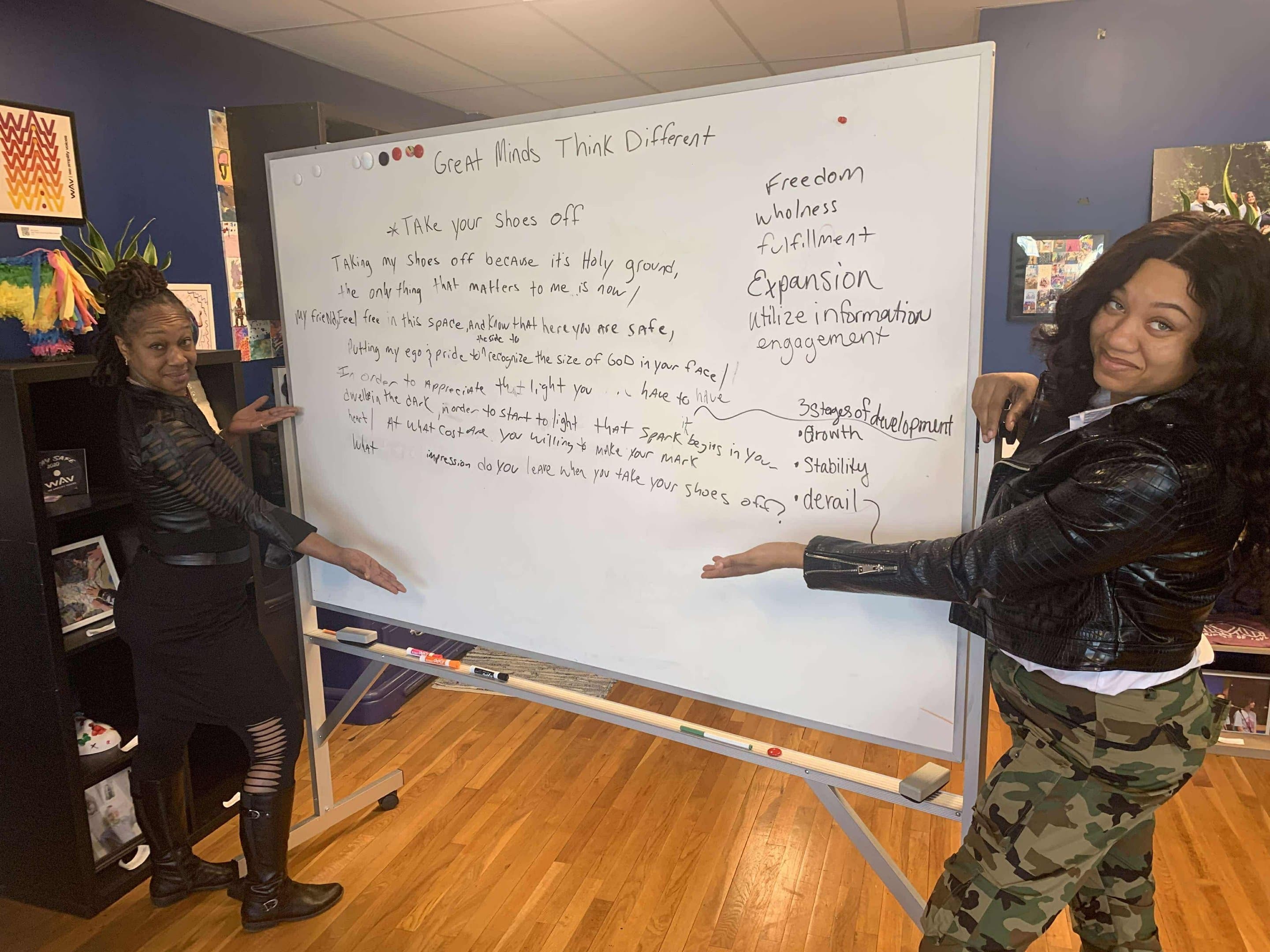Two Poetry Clinic participants presenting writing on a whiteboard